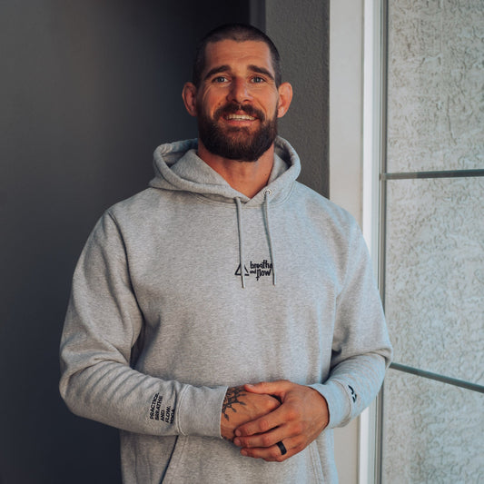 Man wearing a gray hoodie with a logo, standing indoors.
