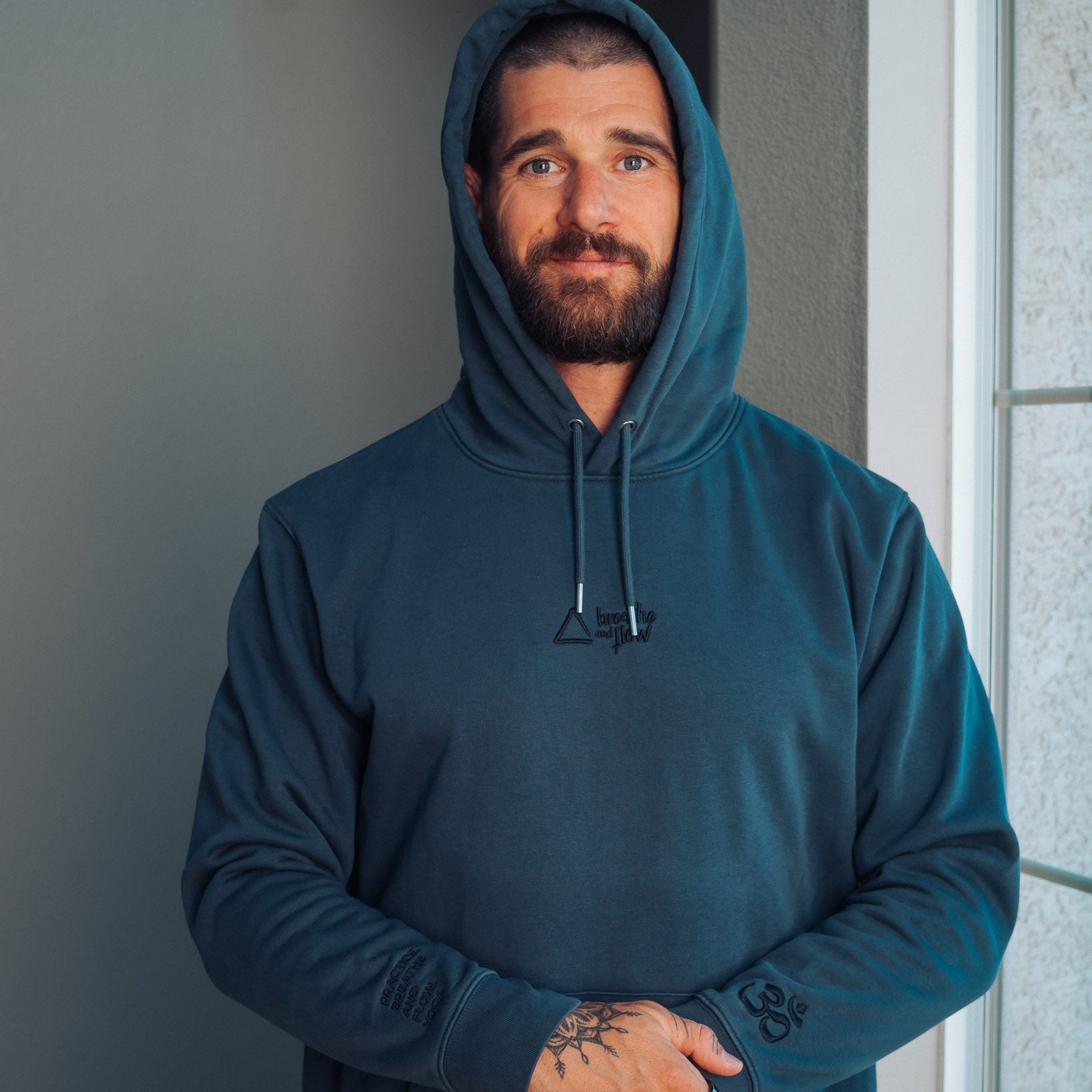 Man wearing a blue hoodie standing indoors against a neutral wall.